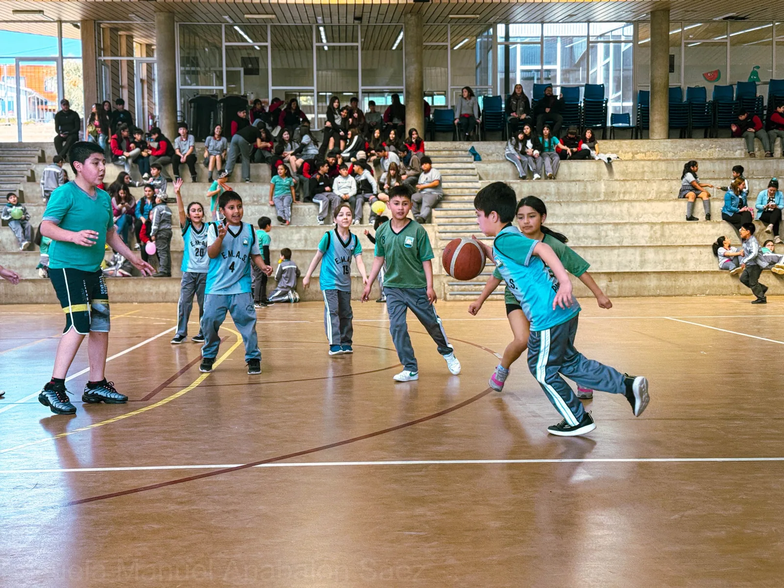 Estudiantes de Educación Básica participando en un partido de básquetbol en el gimnasio de la escuela